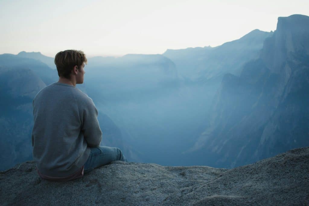 A man sitting in a majestic natural setting, meditating peacefully, surrounded by the beauty of nature.